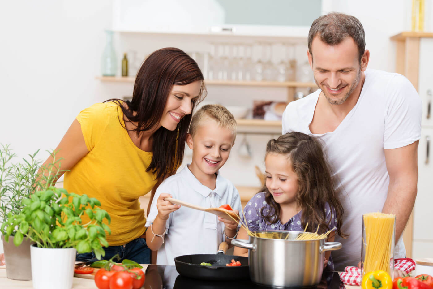 Happy young family with Mom Dad and two young children cooking in the kitchen preparing a spaghetti meal together 1